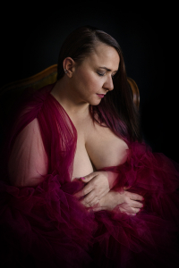 Frau in bordeauxrotem Tüll-Morgenmantel sitzt nachdenklich auf einem Stuhl, Lowkey Boudoir Fotografie, Studio Nina Thilo Fürth
