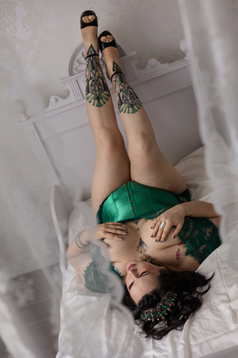 Frau mit dunklen Haaren und einem grünen Korsett liegt im Boudoir Studio Bett, Nina Thilo Fürth
